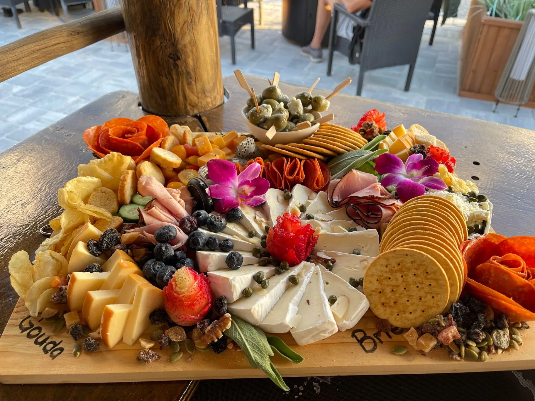 Catering charcuterie board with cheeses, meats, crackers, fruit, and flowers
