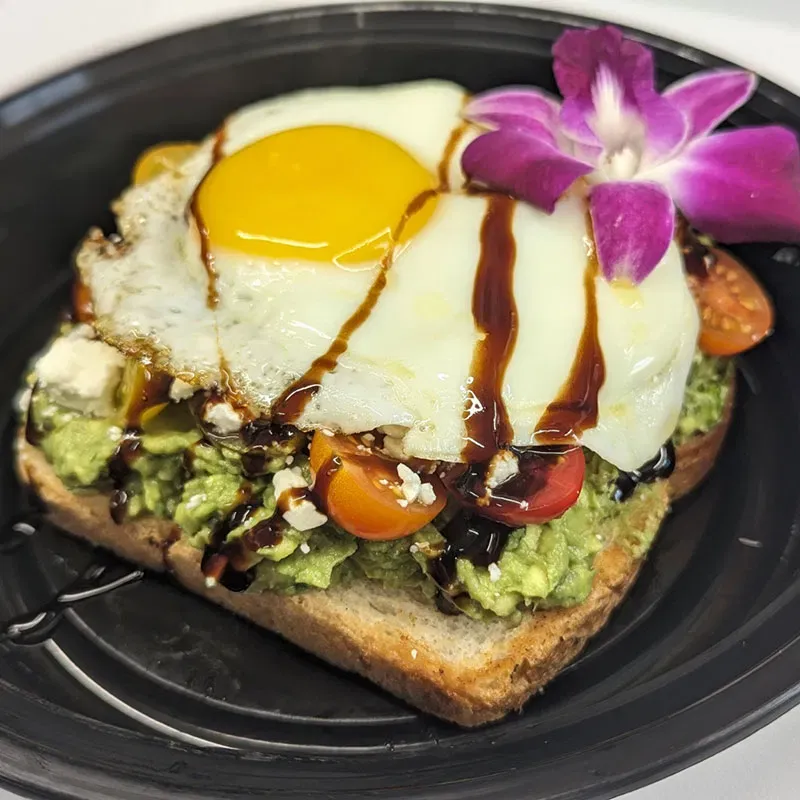 Avocado toast topped with a fried egg, cherry tomatoes, feta, and balsamic drizzle