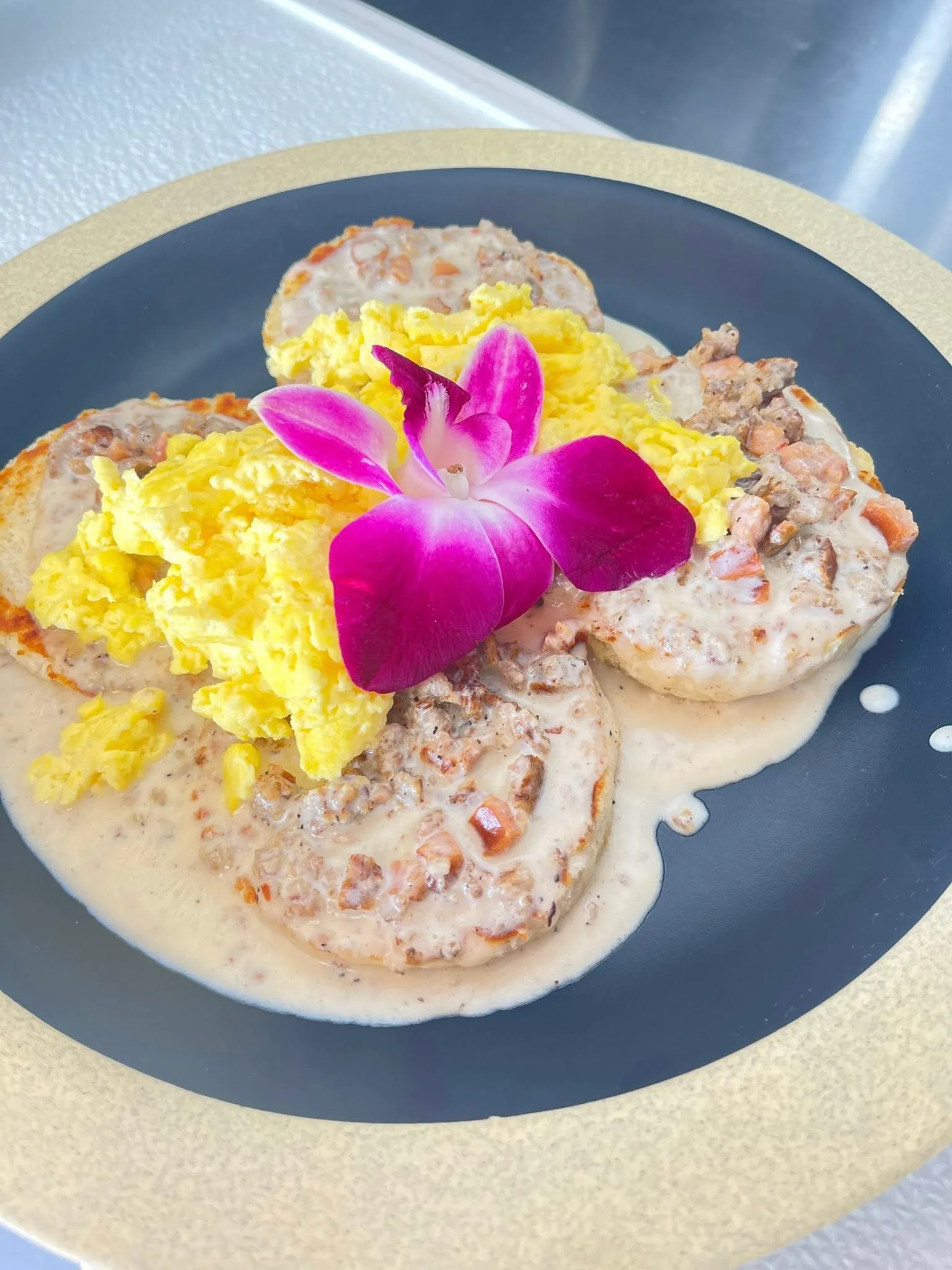 Biscuits and gravy served with scrambled eggs and an orchid garnish